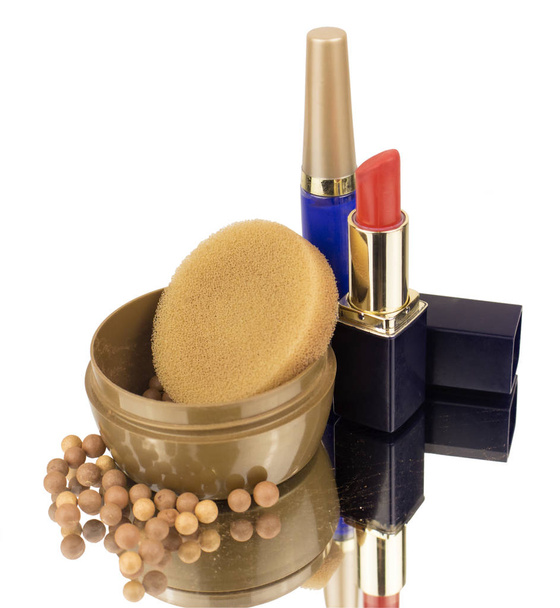 Een set decoratieve cosmetica bestaande uit lippenstift van rode kleur, mascara blauw en poeder van geperste ballen in een ronde pot, tegen de achtergrond van verstrooide bolletjes poeder op een spiegeloppervlak - Foto, afbeelding