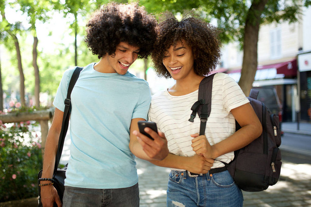 Πορτρέτο των χαμογελαστών νεαρών Αφροαμερικανών φοιτητών κοιτάζοντας κινητό τηλέφωνο - Φωτογραφία, εικόνα