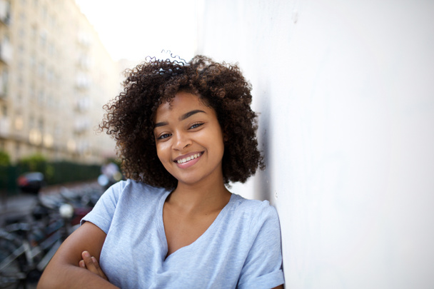 Zbliżenie portret uśmiechniętej młodej Afroamerykanki opierającej się o ścianę na zewnątrz - Zdjęcie, obraz
