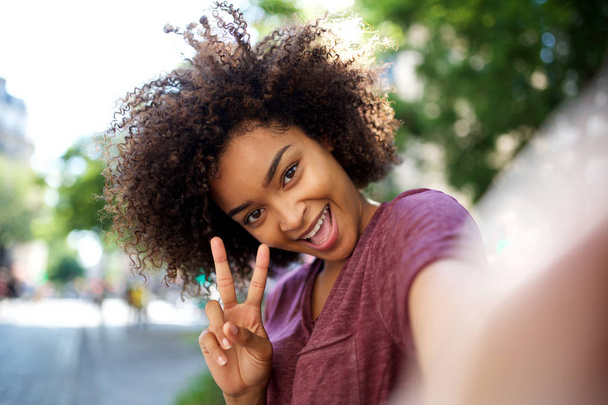 Portrait heureuse femme afro-américaine prenant selfie avec signe de la main de la paix à l'extérieur
 - Photo, image