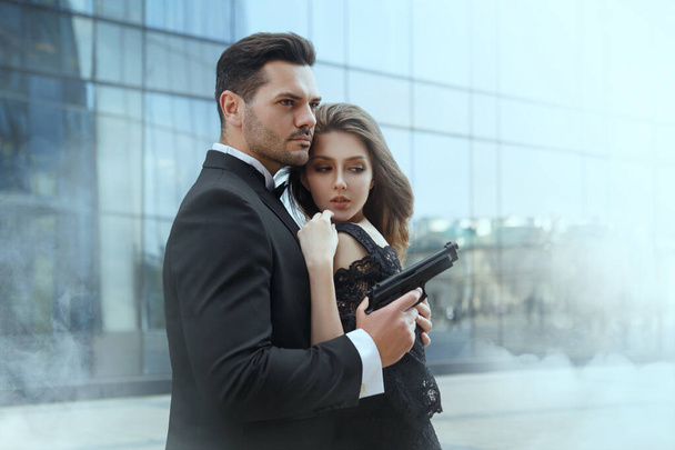 An elegant man with pistols in his hands protects a beautiful girl. - Photo, Image