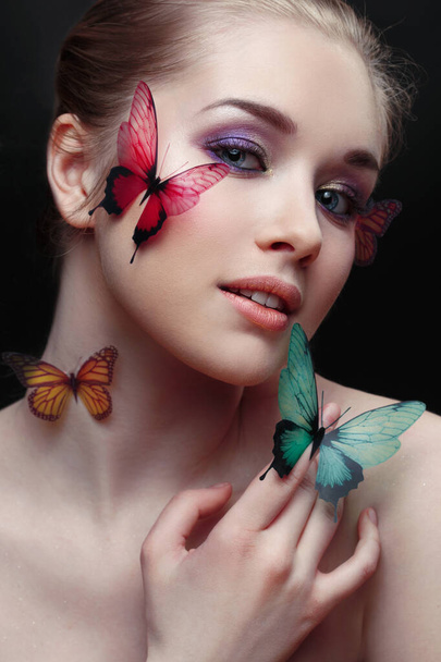 Beauty fashion portrait of cute mysterious girl with butterflies on face and hand on black background. - Фото, изображение