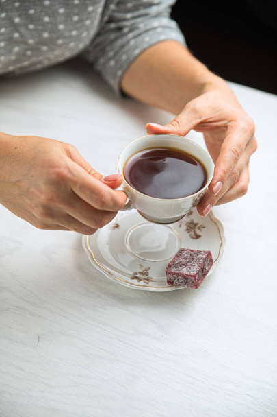 Λευκό φλιτζάνι τσάι πορσελάνη σε λευκό φόντο σε γυναικεία χέρια - Φωτογραφία, εικόνα