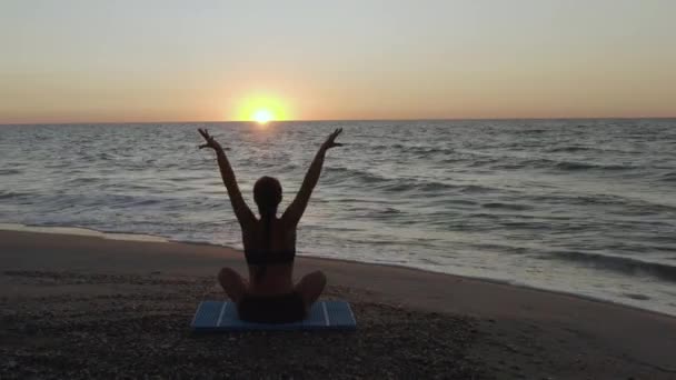 Hermosa joven haciendo yoga sentado en la playa mientras observa el atardecer
. - Metraje, vídeo