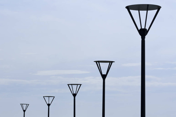 A fekete utcai lámpák sora a halvány szürke ég előtt - Fotó, kép