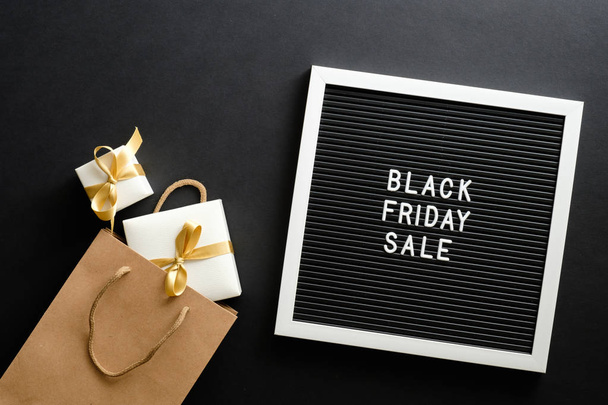 Black Friday sale concept. Letter board with sign "Black Friday sale", shopping bag and gift boxes over black background. Flat lay, top view, overhead. - Fotó, kép