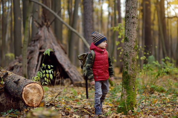 Little boy scout with binoculars during hiking in autumn forest. Teepee hut on background. - Fotoğraf, Görsel