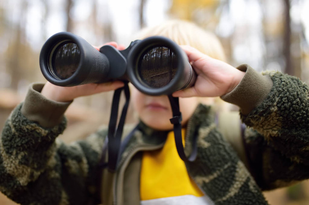 Little boy scout with binoculars during hiking in autumn forest. Child is looking through a binoculars. - Φωτογραφία, εικόνα