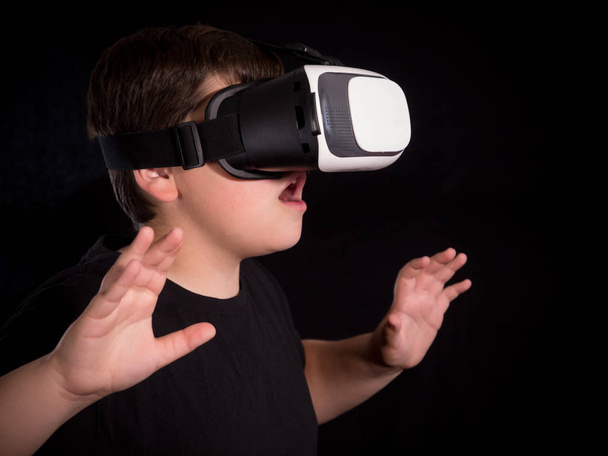 Chłopiec w okularach rzeczywistości wirtualnej zaskoczony tym, co widzi w symulacji lub grze, odizolowany na czarnym tle - Zdjęcie, obraz