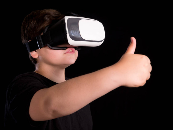 chłopiec w wirtualnej rzeczywistości okulary co symbol ok z jego strony, izolowany na czarnym tle - Zdjęcie, obraz