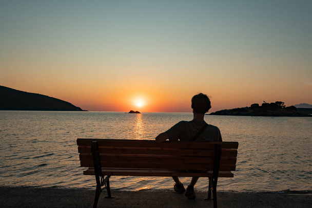 Silhouette eines Mannes, der auf der Bank sitzt und den schönen Sonnenaufgang am Sommerstrand beobachtet - Foto, Bild