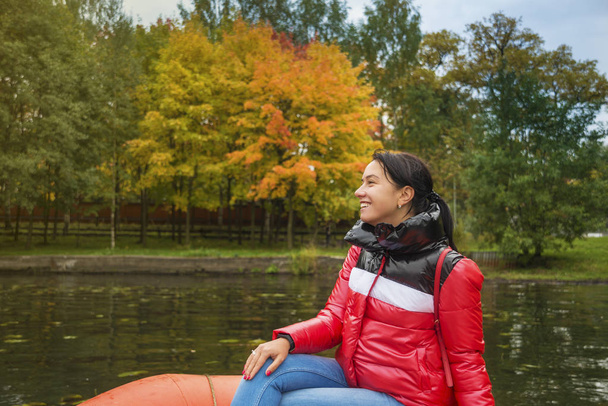 Genç bir kadın sonbahar parkında bir gölette tekneye biniyor. - Fotoğraf, Görsel