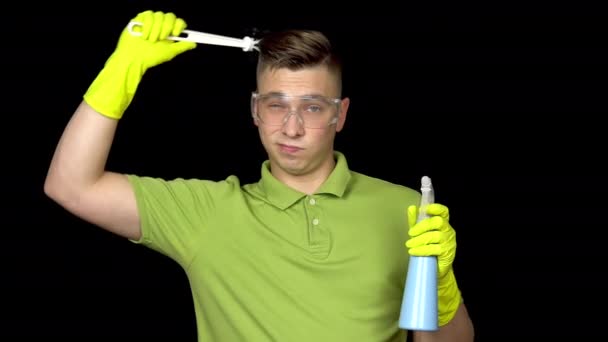 Um jovem coça a cabeça com uma escova de vaso sanitário e uma ideia lhe ocorre. Homem de óculos de segurança e luvas para limpar o banheiro. O tipo tem uma escova de sanita e spray. Em um fundo preto
 - Filmagem, Vídeo