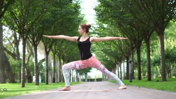 A young girl stands in a yoga pose in a park alley in slow motion - 映像、動画