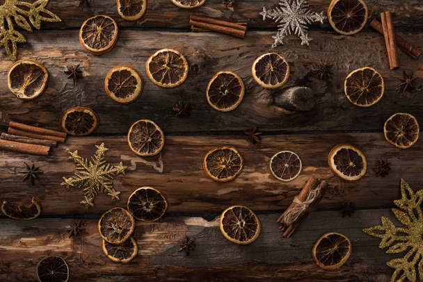 bovenaanzicht van gedroogde citrusschijfjes met anijs, kaneelstokjes en decoratieve sneeuwvlokken op houten ondergrond - Foto, afbeelding