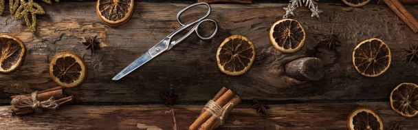 pohled shora na skořicové tyčinky, anýz, sušené citrusové plátky, nůžky a sněhové vločky na dřevěném pozadí, panoramatický záběr - Fotografie, Obrázek