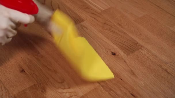 A hand washes a brown laminate floor with a yellow rag with a spray in beige protective gloves. Cleaning and disinfection in offices and apartments - Video