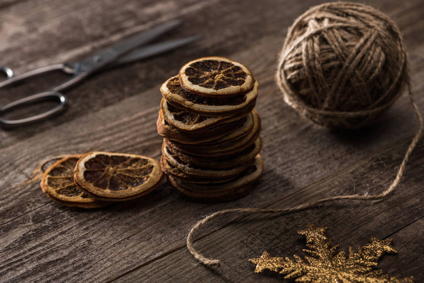 selective focus of thread, scissors and dried citrus slices, snowflake on wooden background - Foto, Imagem