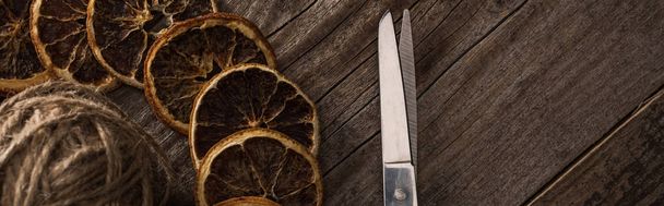 вид сверху на нить, ножницы и сушеные цитрусовые ломтики на деревянном фоне, панорамный снимок
 - Фото, изображение