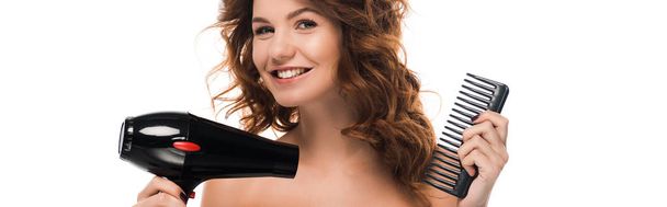 plano panorámico de chica rizada feliz sosteniendo secador de pelo y cepillo aislado en blanco
  - Foto, Imagen