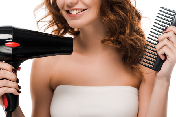 vista cortada da menina feliz usando secador de cabelo enquanto escova o cabelo isolado no branco
  - Foto, Imagem