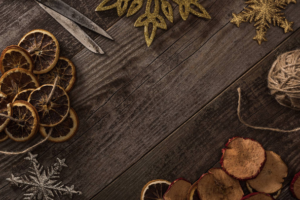 top view of dried citrus and apple slices near snowflakes, rope and scissors on wooden surface with copy space - Photo, Image