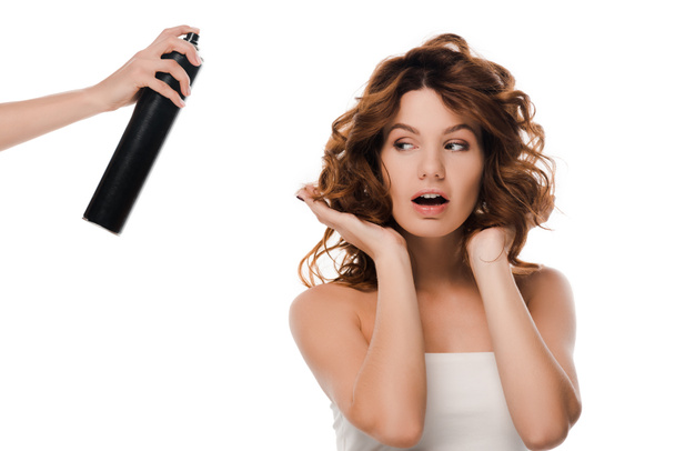 περικοπή άποψη της γυναίκας που κατέχουν μπουκάλι σπρέι μαλλιών κοντά ελκυστική σγουρά κορίτσι που απομονώνονται σε λευκό  - Φωτογραφία, εικόνα