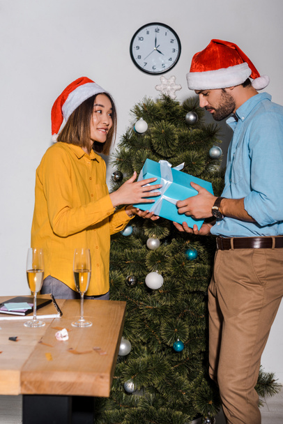 glücklich bärtiger Mann gibt Geschenk an asiatische Frau mit Weihnachtsmann  - Foto, Bild