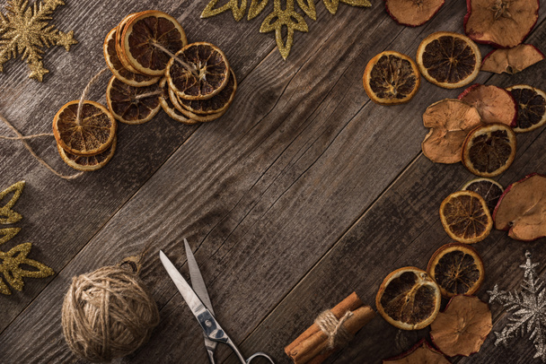 top view of dried citrus and apple slices near snowflakes, scissors, thread and cinnamon on wooden surface with copy space - Фото, зображення