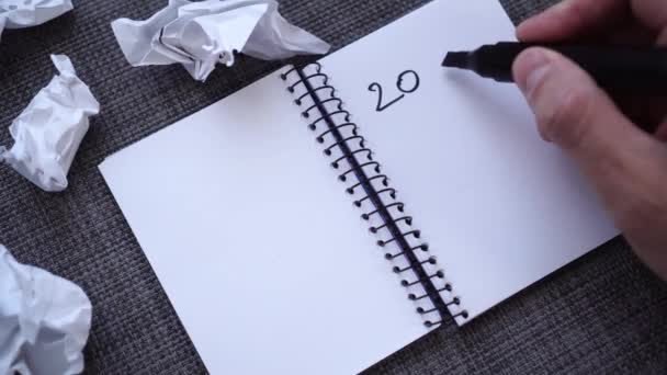 A male hand writes 2020 GOALS in a notebook on a gray textured table surface. Tears out the page and throws. Crumpled sheets of paper are nearby. The concept of a complex creative search for planning in the new year - Séquence, vidéo