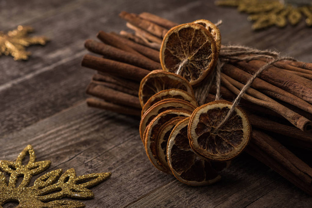 dried citrus slices on thread near cinnamon and snowflakes on wooden background - 写真・画像