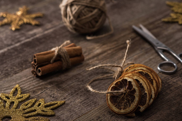 selective focus of dried citrus slices on thread near cinnamon, scissors and snowflakes on wooden background - Photo, Image