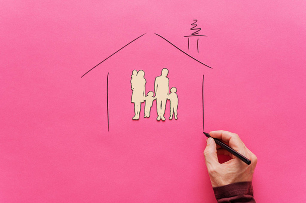 Male hand drawing a house shape around a paper cut family silhou - Foto, afbeelding