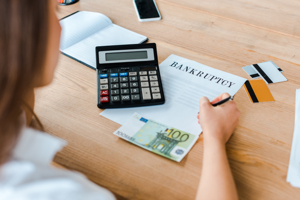 selective focus of woman signing document with bankruptcy letters near credit cards and calculator  - Foto, Bild