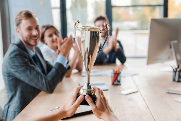 cropped view of businesswoman holding champion cup near coworkers in office  - Photo, Image