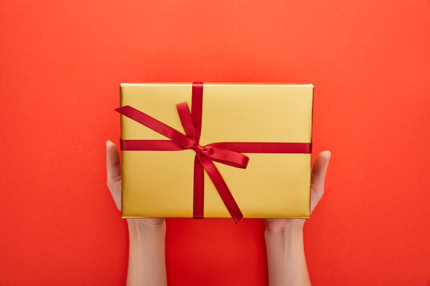 обрезанный вид женщины, держащей золотую подарочную коробку на красном фоне
 - Фото, изображение
