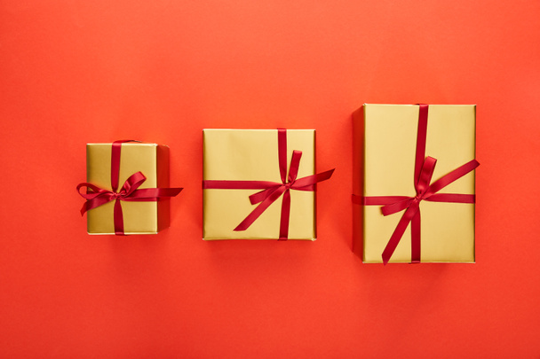 flat lay with three golden gift boxes on red background - Foto, imagen