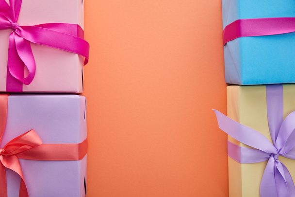 vista superior de cajas de regalo multicolores con cintas y arcos sobre fondo naranja con espacio para copiar
 - Foto, Imagen