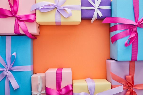 square frame of multicolored gift boxes with ribbons and bows on orange background with copy space - Photo, Image