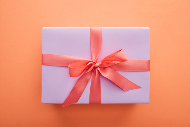 top view of violet gift box with red ribbon and bow on orange background - Fotoğraf, Görsel