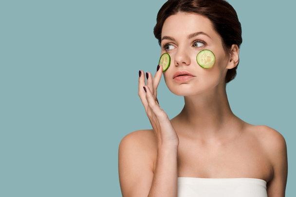 attractive woman touching cucumber on face isolated on blue  - Photo, Image