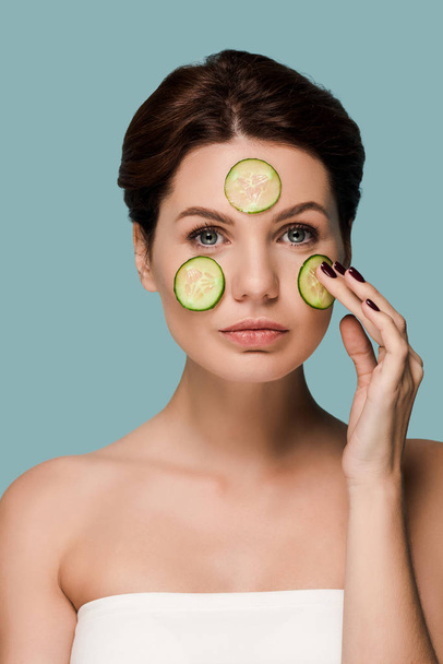 young attractive woman touching cucumber on face isolated on blue  - Photo, image