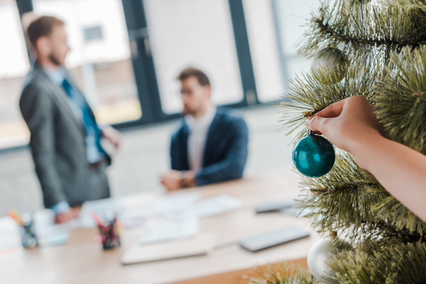 cropped view of woman touching christmas ball on christmas tree near businessmen in office  - Photo, Image
