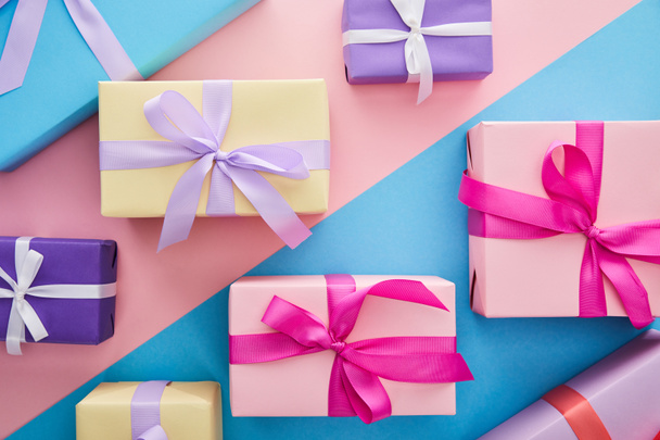 πάνω όψη πολύχρωμα κουτιά δώρων με κορδέλες και φιόγκους σε μπλε και ροζ φόντο - Φωτογραφία, εικόνα