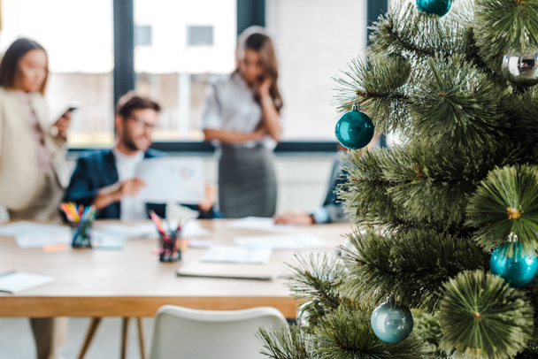 a díszített karácsonyfa szelektív fókusza az irodai multikulturális munkatársak közelében   - Fotó, kép