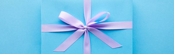 top view of blue gift with violet ribbon on blue background, panoramic shot - Фото, зображення