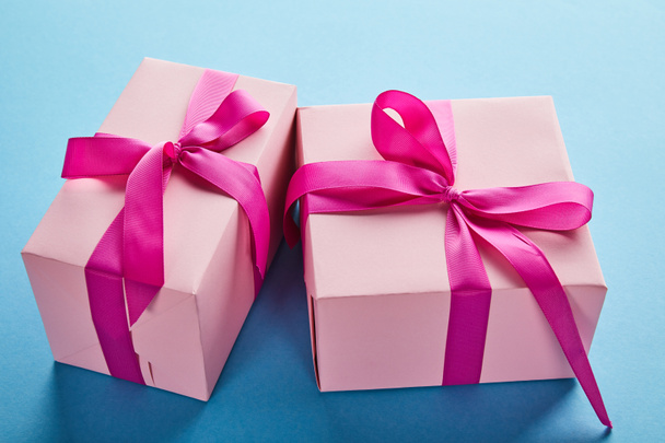 różowe kolorowe pudełka z karmazynowymi wstążkami i kokardkami na niebieskim tle - Zdjęcie, obraz