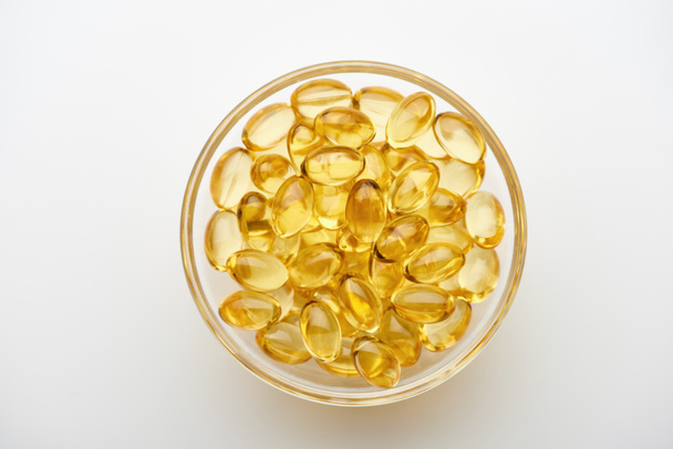 bovenaanzicht van gouden visolie capsules in glazen schaal op witte achtergrond - Foto, afbeelding