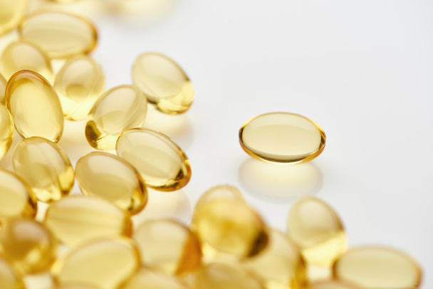 close up view of golden fish oil capsules scattered on white background - Φωτογραφία, εικόνα