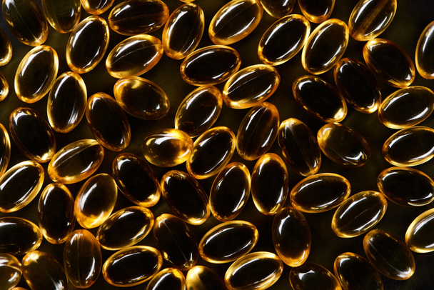 vista dall'alto di capsule di olio di pesce dorato su sfondo nero in scuro
 - Foto, immagini